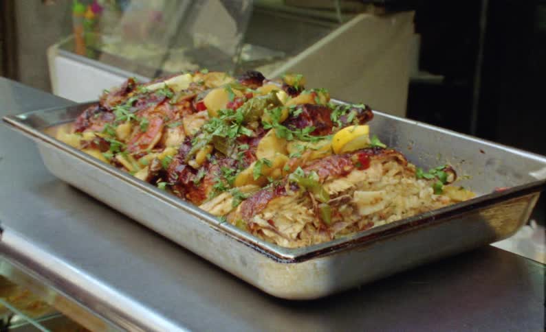 A meat food with some vegetables and potatoes in a metal pan on a metal table