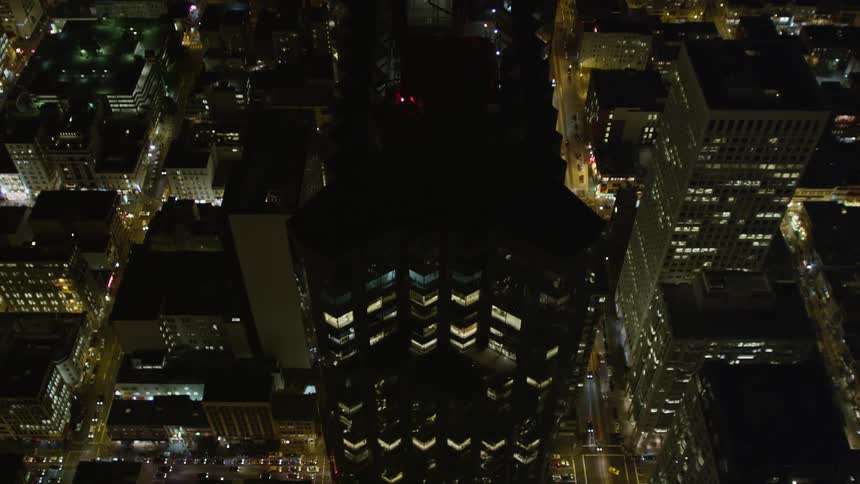 Aerial panorama of a modern mirrored skyscraper in the middle of an illuminated metropolis at night