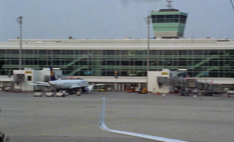 A large passenger airplane is parked on an airport tarmac caught on vintage film
