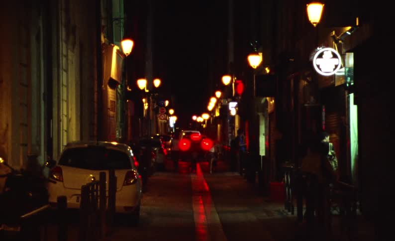 Pedestrians walk a narrow city street at night
