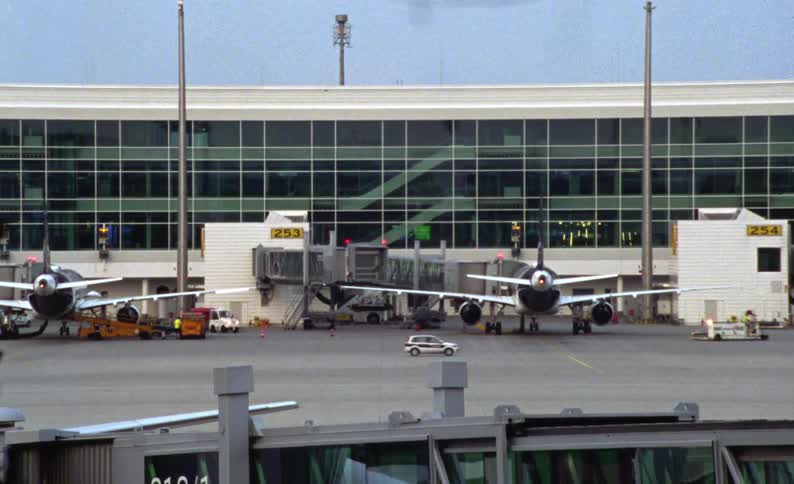Some small planes parked next to a building at an airport with some vehicles passing by