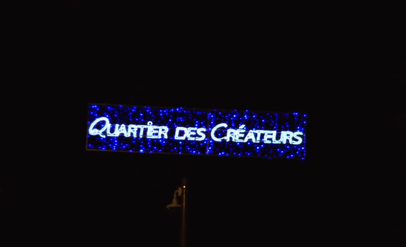 A large sign in a city at night and it is illuminated with blue leds and white text