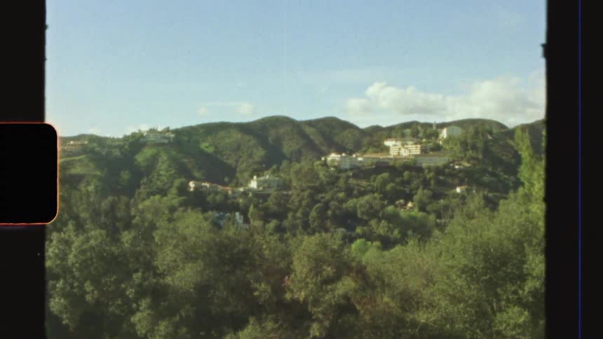 Film footage shows a valley containing some buildings and many trees