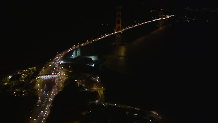 Aerial panorama of a highway with vehicle traffic connecting to a bridge over the sea in a metropolis at night