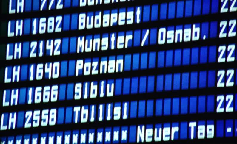 A large monitor with city and time information written in white on a blue background