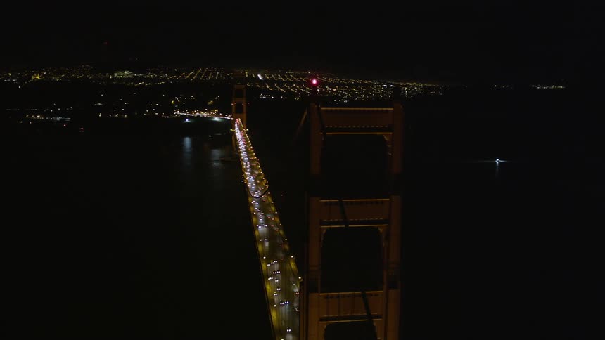 An aerial view of a bridge at night with many cars passing over it