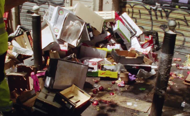 Boxes of vegetables and fruits thrown on the ground on a sidewalk in the city street