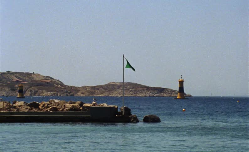 Landscape of a crossing next to rocks on the sea coast with a green flag and viewpoint on the horizon