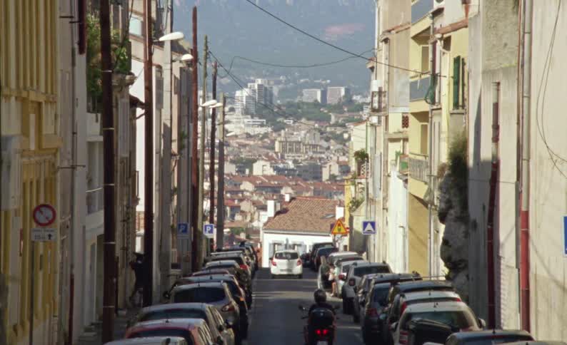 Street of a suburban city with parked vehicles and a city in the background