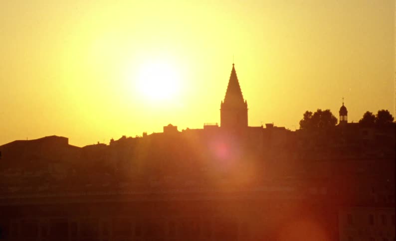 Urban city with old buildings on the edge of a river canal with docks and boats and in the background a cathedral illuminated by the sunset