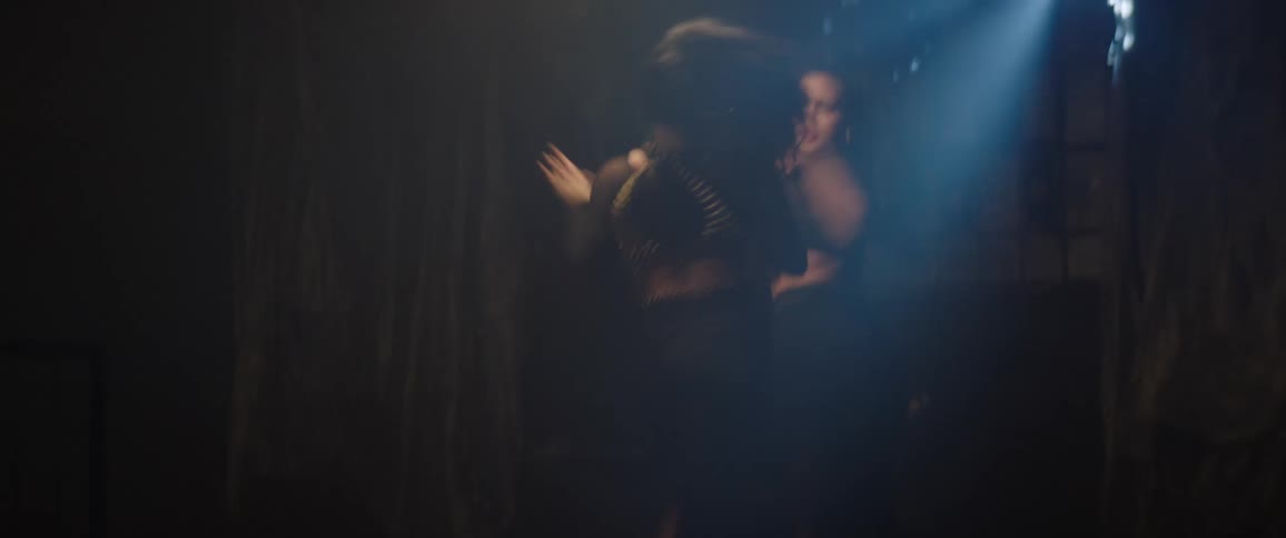 Two women are in a dark place with a crack of light and they are dancing
