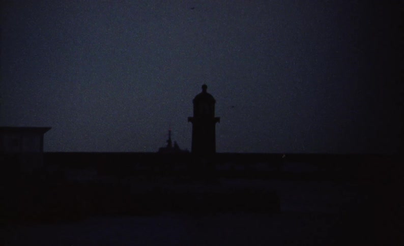 Silhouette of a lighthouse at night with a bright green light flashing
