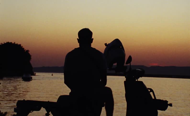 A man is sitting by the water watching the sunset