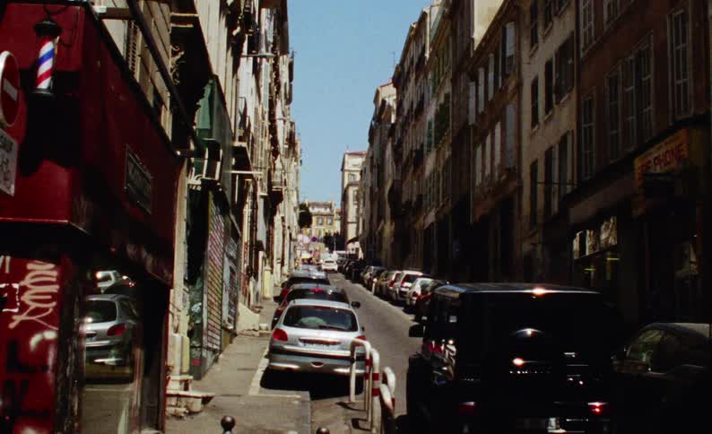 Suburban street with vehicles parked on the sides and a car driving up through the city