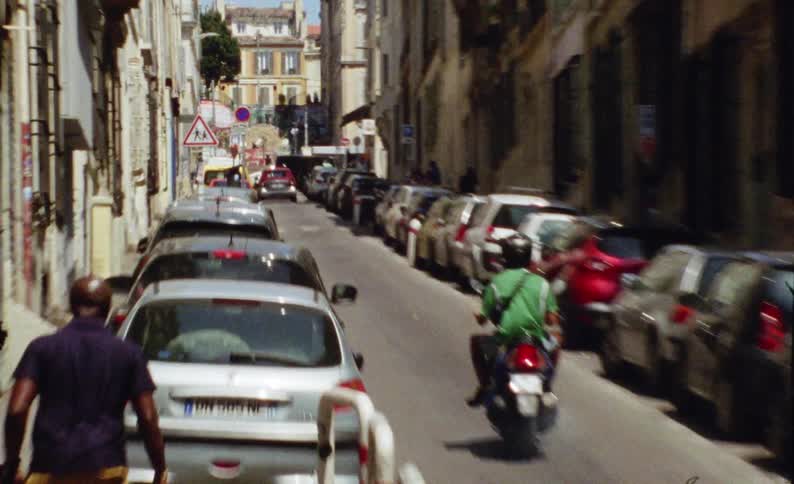 Street of an urban city with a ramp and rise of parked vehicles and motorbikes traveling
