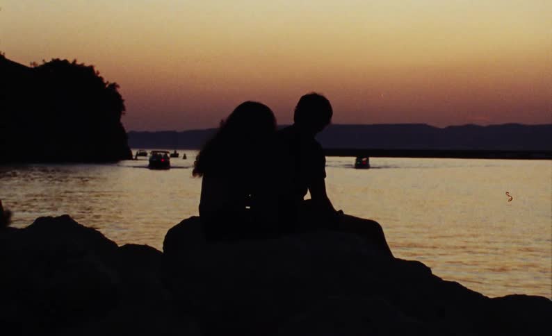 Silhouette of a couple sitting on the stone by the sea with the red sky in the late afternoon