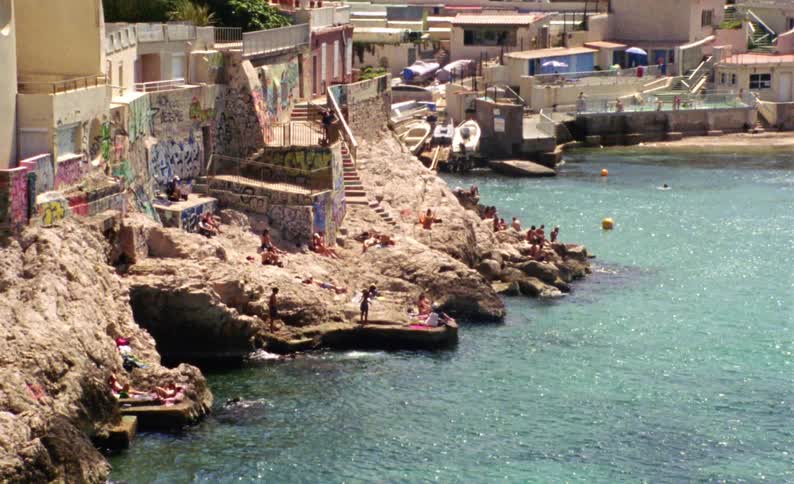 Turquoise blue beach with sunbathers on the edge of an old urban town
