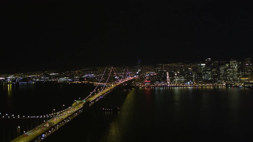 Aerial panorama of a metropolis with a skyscraper and a long bridge illuminated at night with vehicle traffic