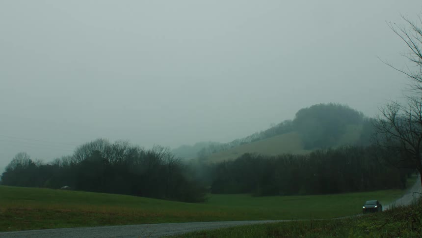 Black sports car passing at high speed through a narrow street next to fields and mountains on a cloudy day