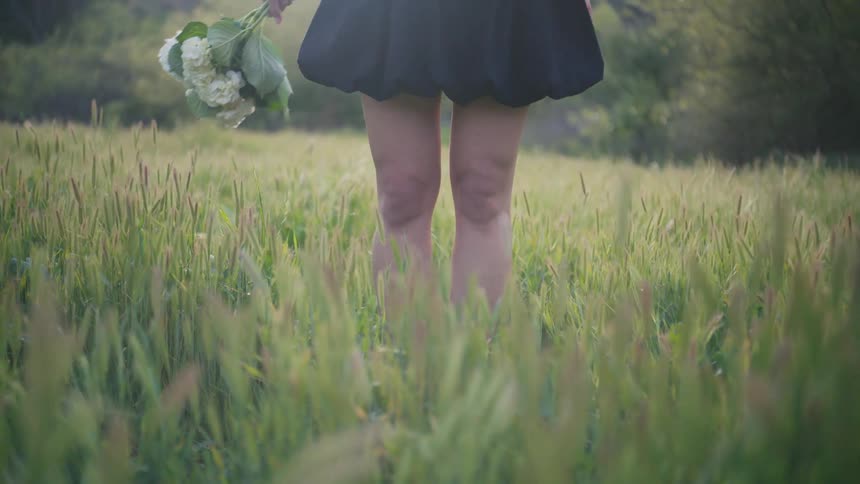 Womans hands holding a bouquet of flowers while wearing a black dress in a field with grass and trees around