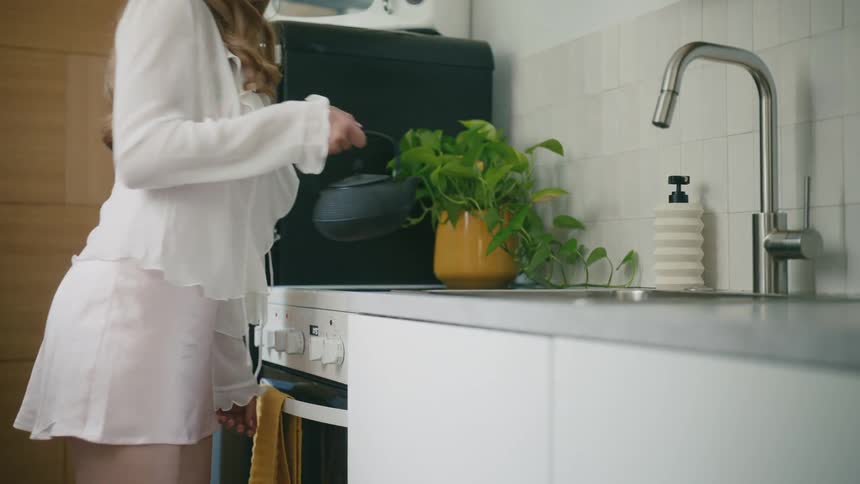 Woman picking up a kettle from the stove in the kitchen