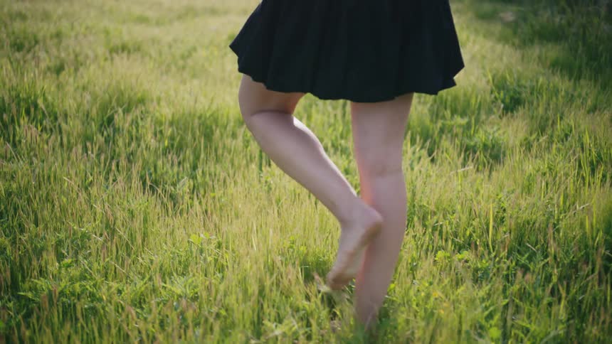 Barefoot woman holding a bouquet of flowers walking through a field with green grass