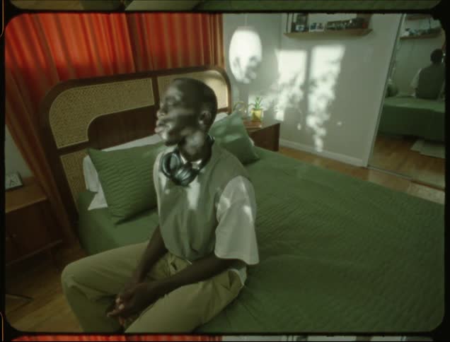 Man sitting on bed with eyes closed and sunlight reflecting on his face