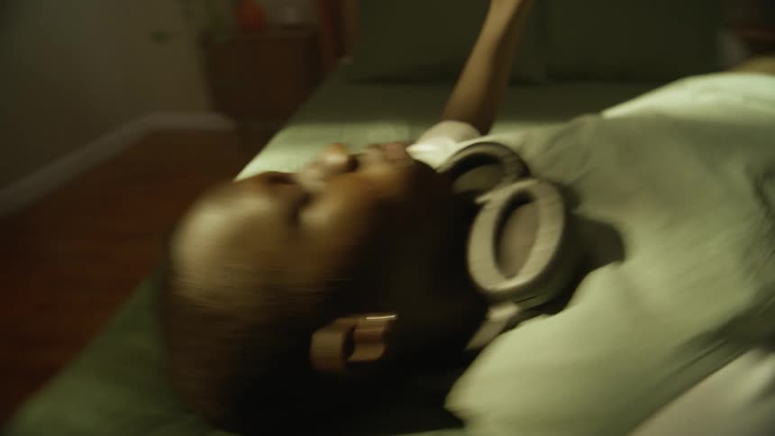 A black man with headphones lying on a bed