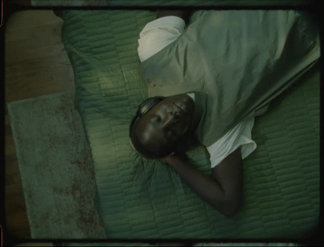 A teenage boy lies on his bed listening to music through headphones