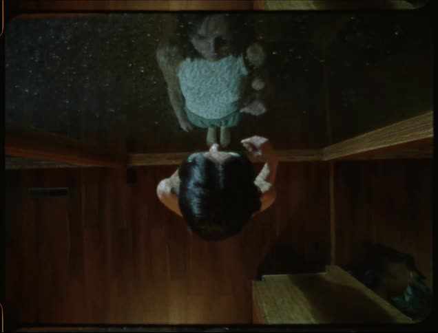 Woman walks across wooden floor and stands with a hand on the glass while looking out at rain
