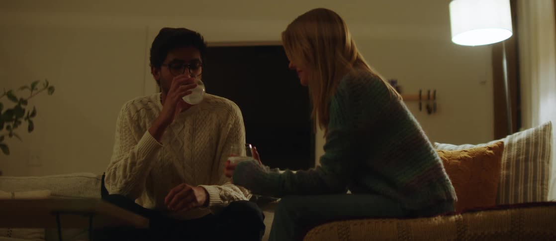 A man and a woman sit on the couch and talk while drinking white wine