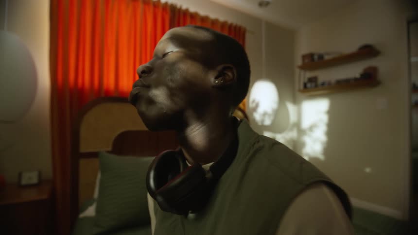 Side portrait of a man sitting in bed with his eyes closed and headphones around his neck