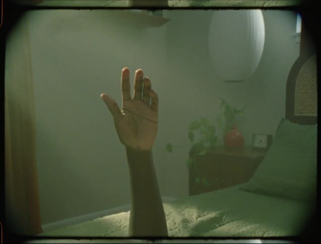 A black man raises his forearm off of a bed