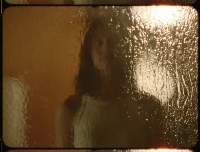 A woman walks up to a rain soaked window and puts her hand on the glass
