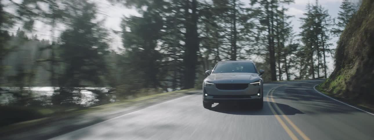 A car drives on a road next to a forest and body of water