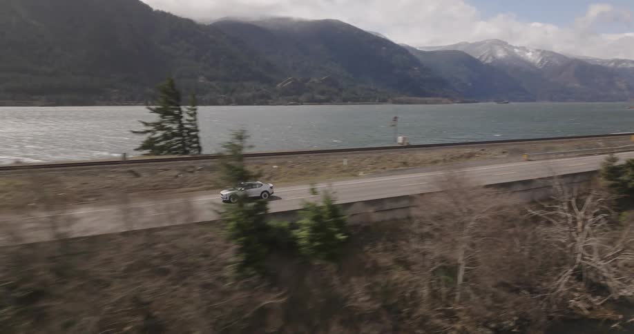 Aerial panorama of a white car crossing a bridge over the sea in a natural environment with mountains around