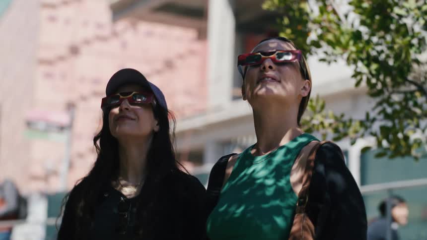 Two women wearing sunglasses looking up under a tree in the city