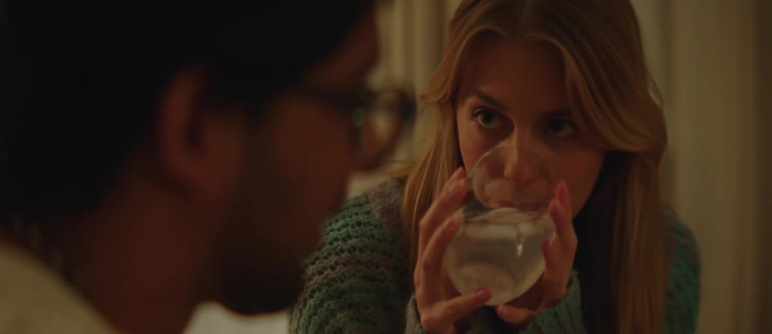 A woman drinks white wine as the man accompanying her speaks