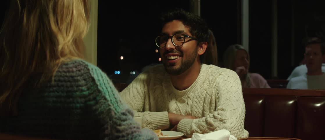 A man and a woman are sitting at a restaurant in front of each other talking and the man smiles