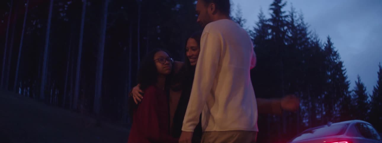 A family of three hugs by the side of a forest road