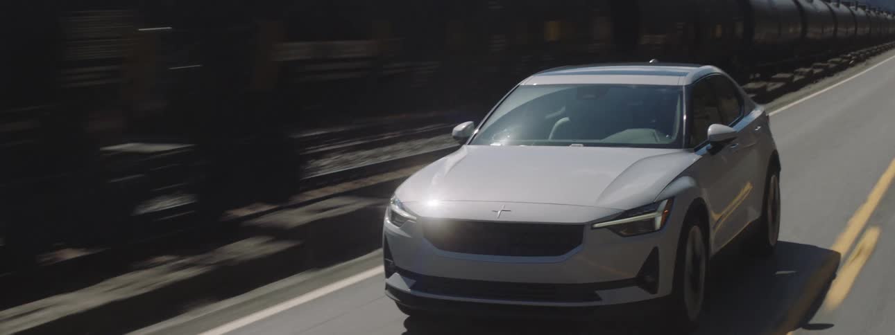 White suv sports car traveling along a paved road next to a freight train during the day