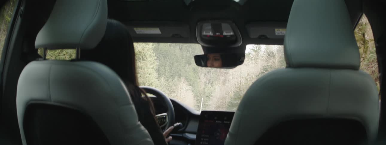 Interior view of a vehicle with a woman driving during the day in a natural environment