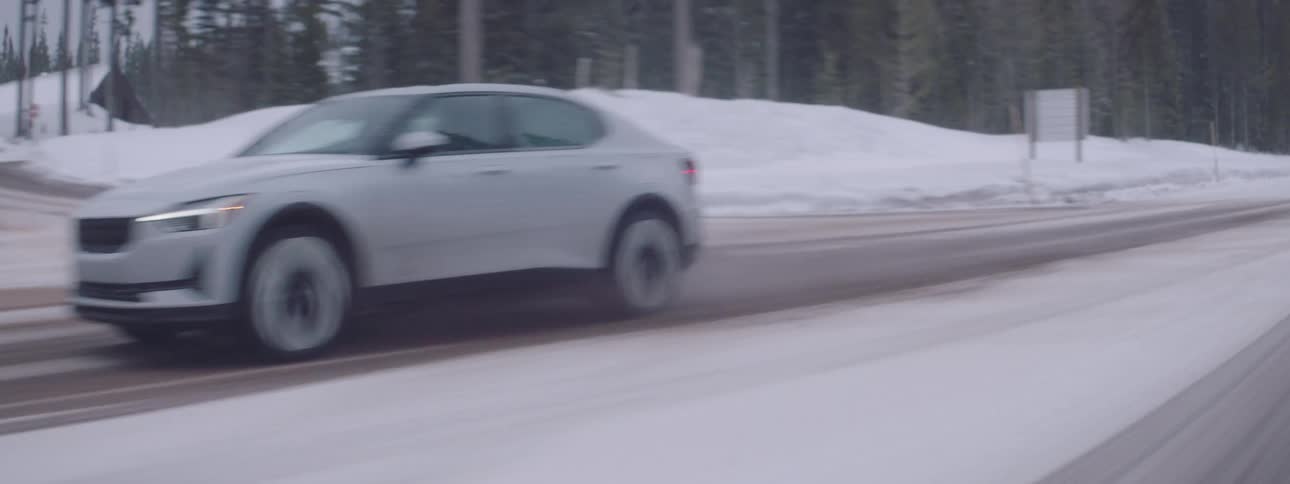 A white car driving on a road and around it there is a lot of snow and trees