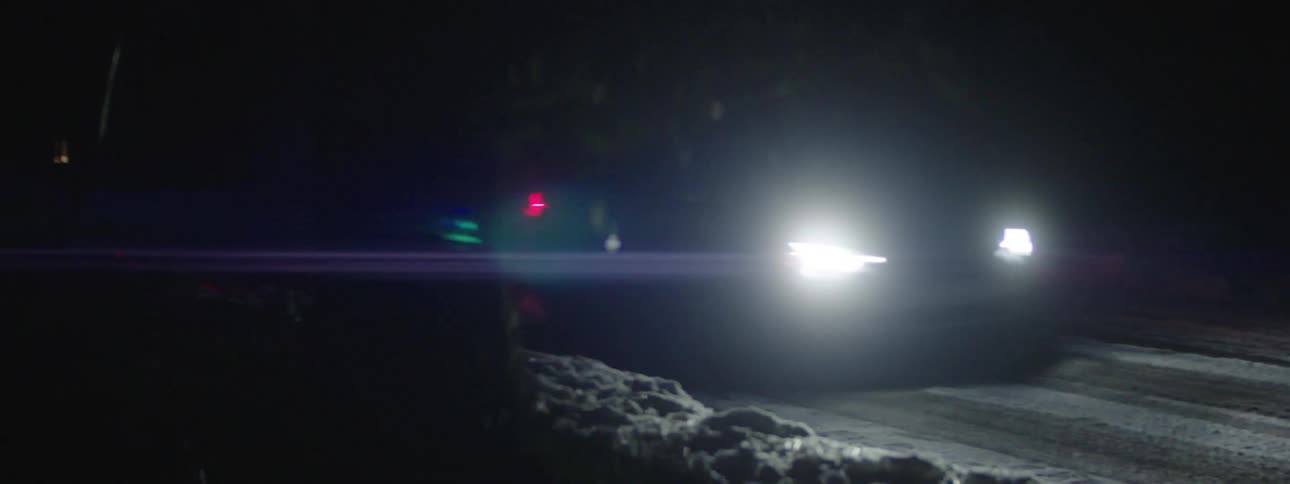 A car with headlights on driving on a snowy road at night