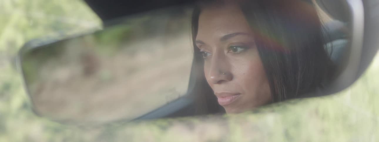 A reflection on a rearview mirror of a sad woman driving a car