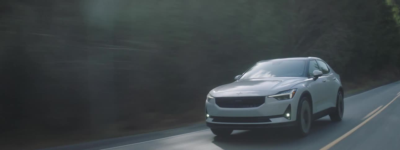 White suv car moving along an asphalt road next to trees vegetation