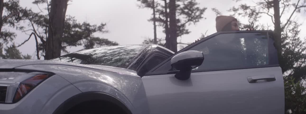 Woman getting out of the car that is parking in an outdoor environment with trees around