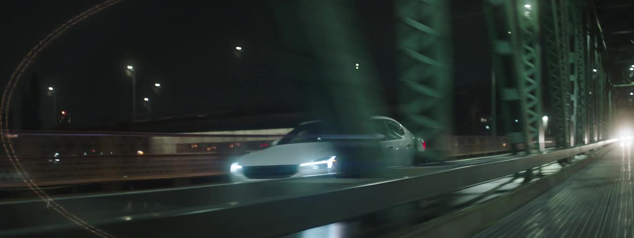 A white car driving down a street at night and some lights reflecting on the surface of the bodywork
