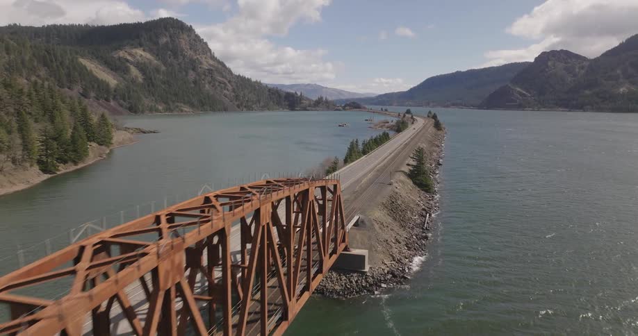Aerial view of a car driving on a land bridge over a lake in the mountains