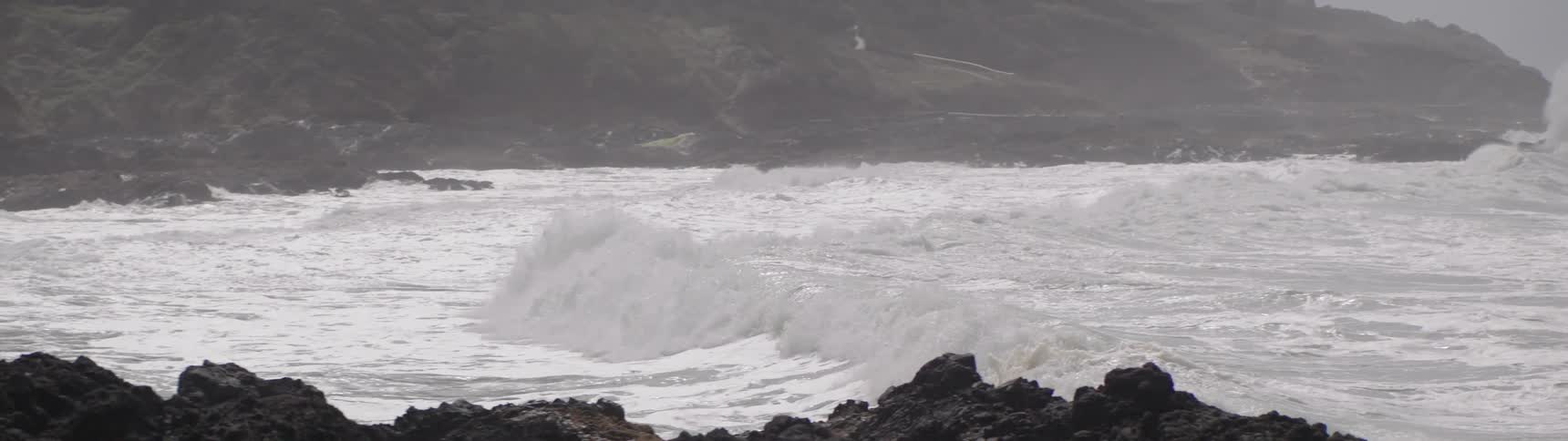 Sea waves breaking near the beach sand with rocks and shores around and on a cloudy day